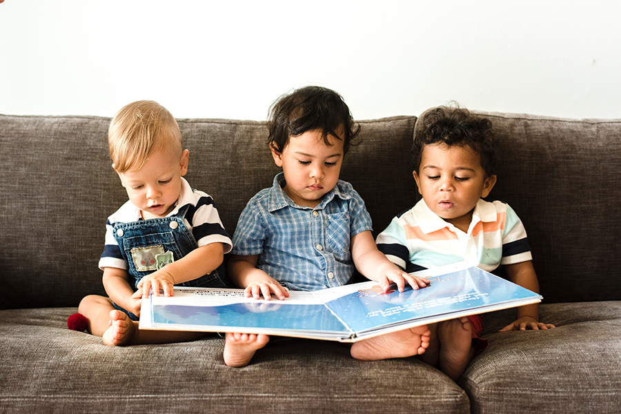 Three infant children looking in a large board book