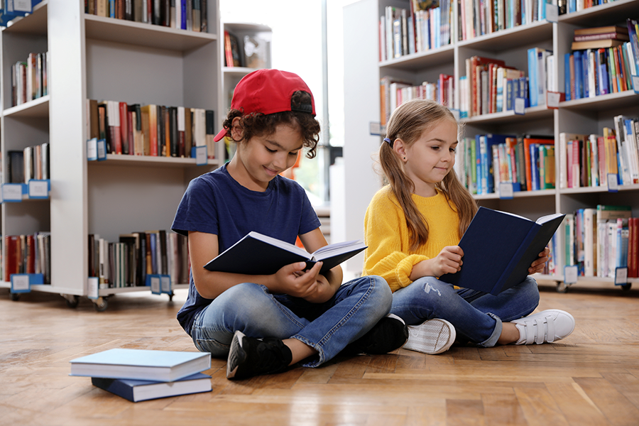 Young girl and boy sitting on library floor reading