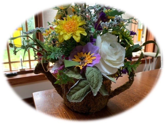 Floral arrangement in a wicker and moss watering can container. 