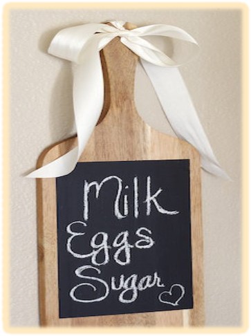 Wooden cutting board with handle, black chalkboard contact paper rectangle glued on with a white bow on the handle. 