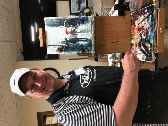 Man smiling next to a paint set and easel. 