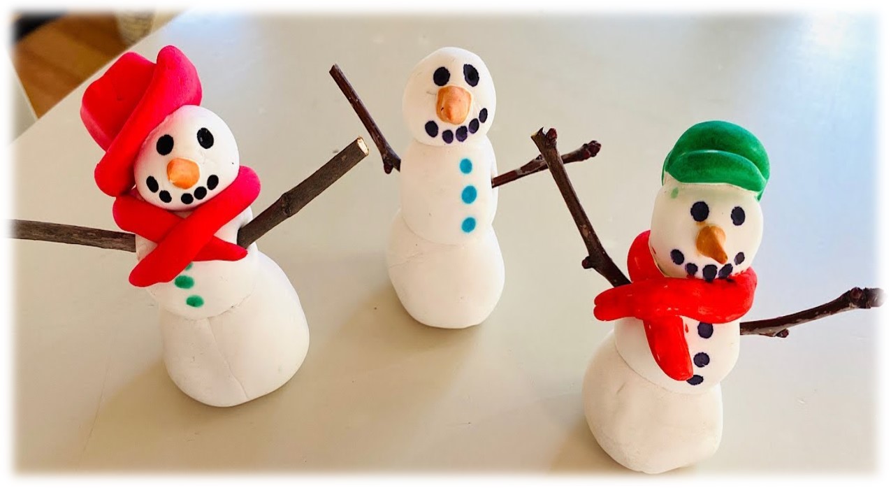 Three small white snowmen made from clay. They have stick arms, black painted dots for eyes, mouths and buttons. Two have red scarves. One snowman has a green hat another has a read hat. Each has and orange carrot-shaped nose.  