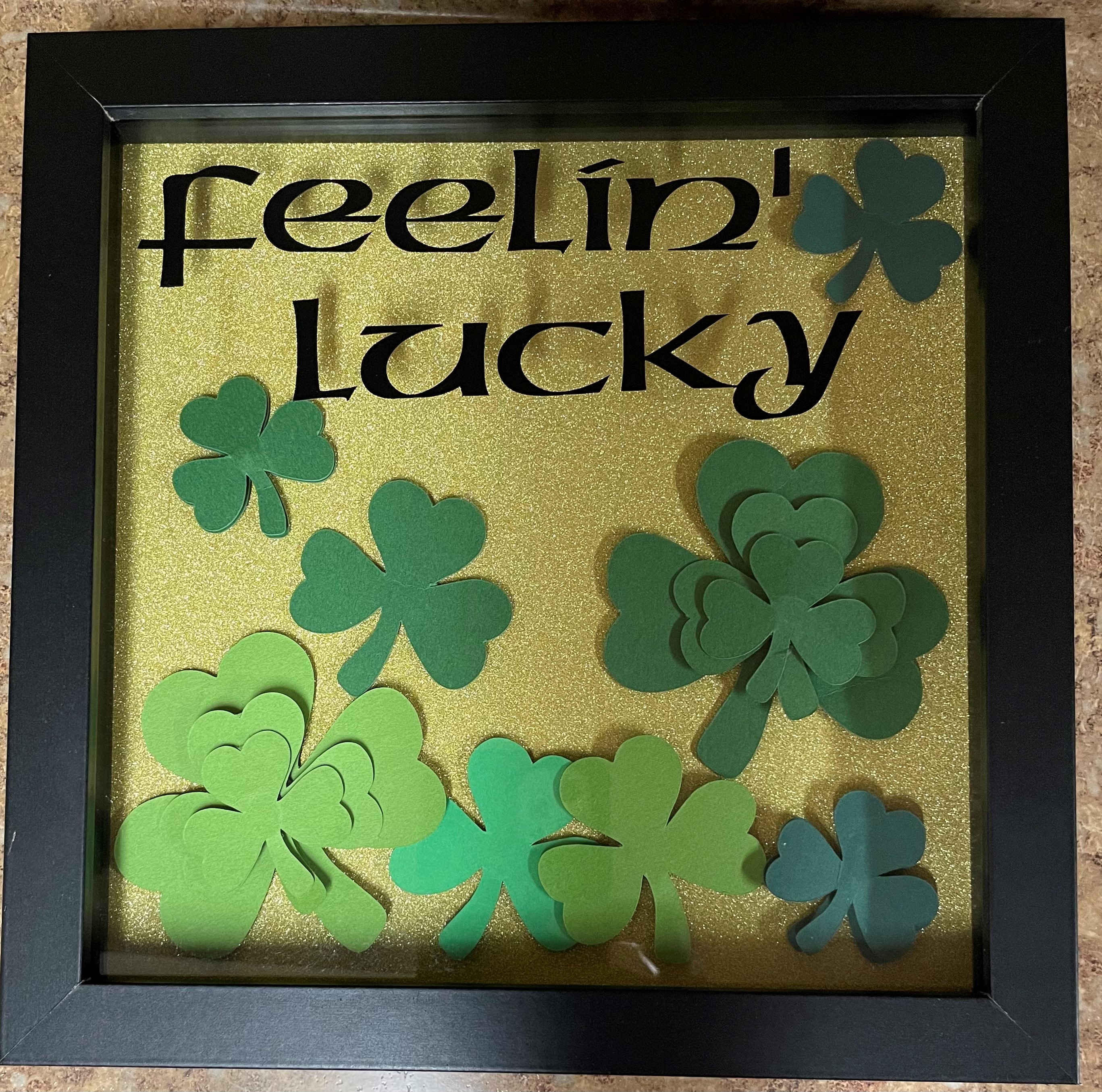 "Feeling Lucky" with shamrocks and a gold background in a shadow box