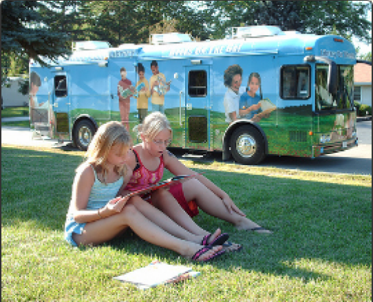 Two girls reading on the lawn in front of the bookmobile