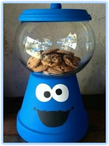 Cookie jar base is a terra cotta pot painted blue with a monster face, a clear round bowl sits on the base with a terra cotta dish topping it all. 