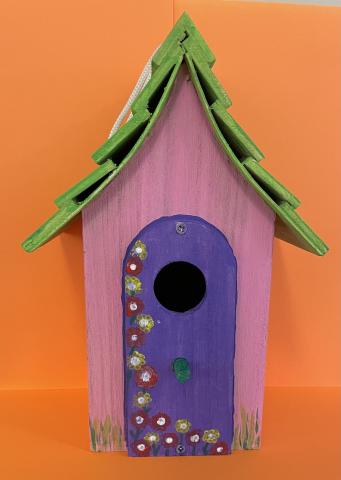 Image: a pink and green birdhouse with a purple door. 