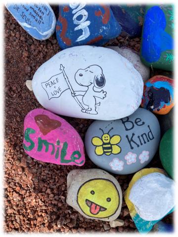 Rocks painted with Snoopy, a bee, and a smiley face with tongue sticking out. 