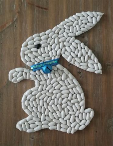 SIDEWAY FACING BUNNY COVERED WITH WHITE BEANS, BLUE COLLAR AND BELL.