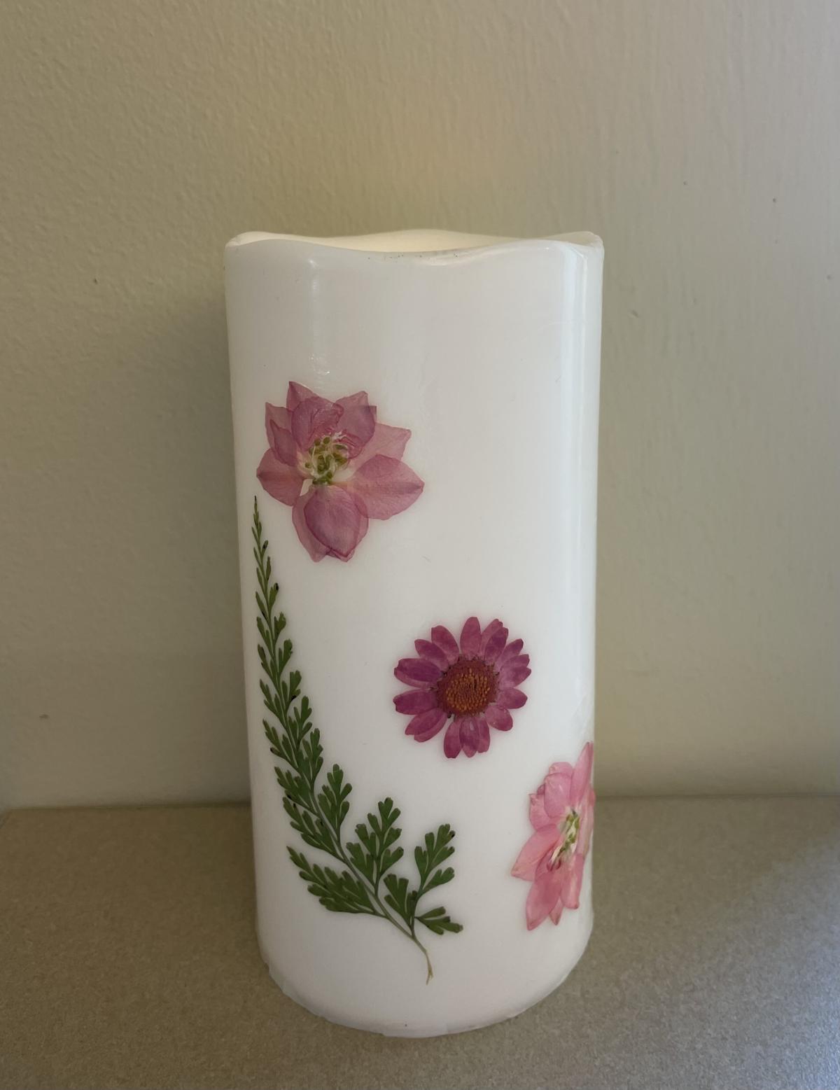 White candle with embedded flowers and greens.