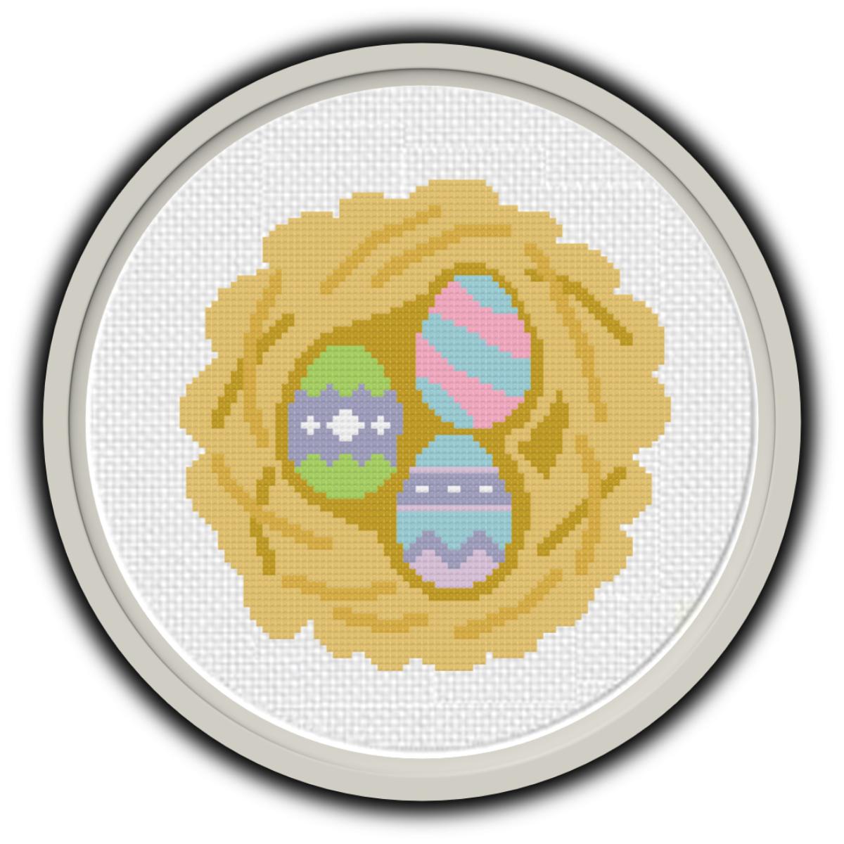 Gray frame with cross stitch light brown nest and three multicolored eggs in nest. 