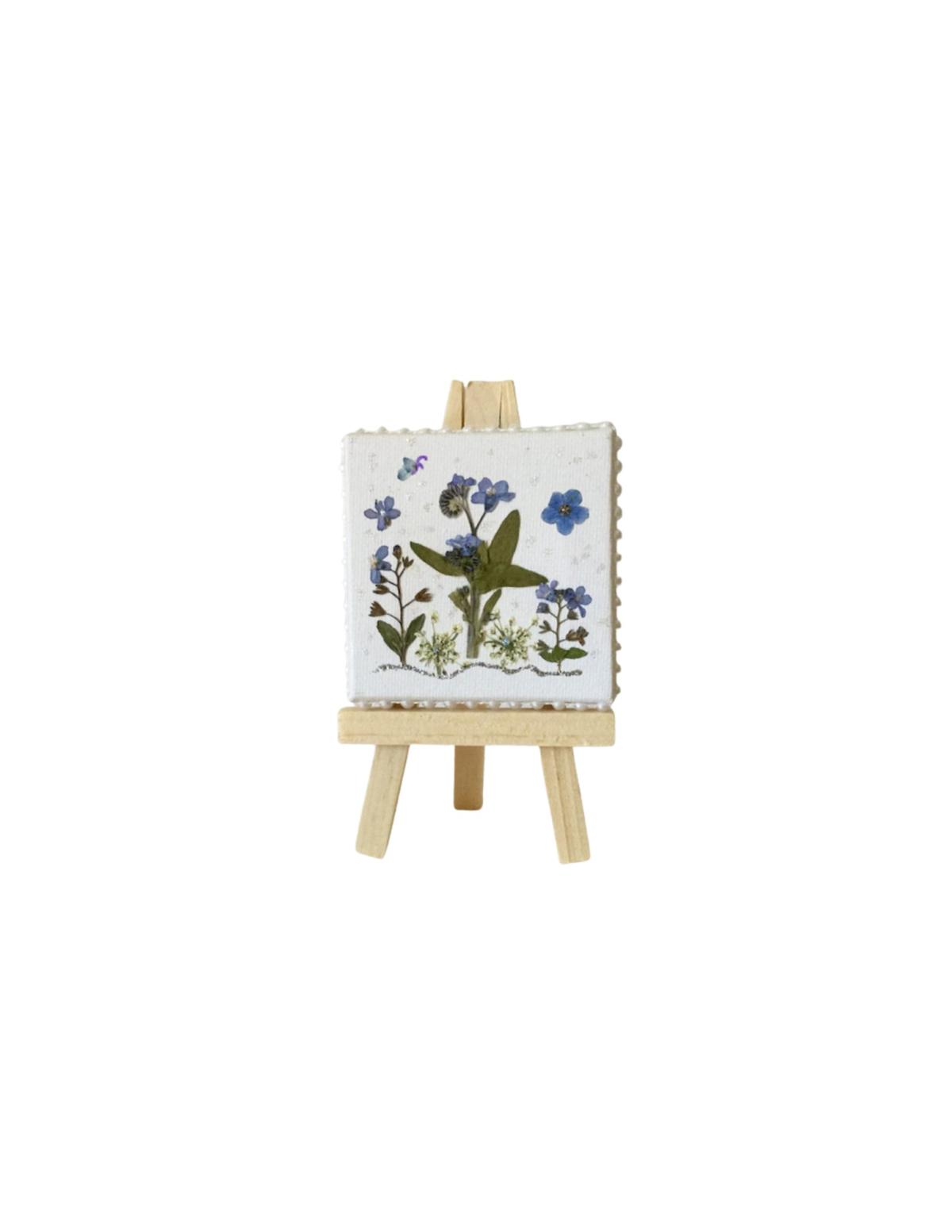 White tile with purple flowers and green leaves on a wooden easel.