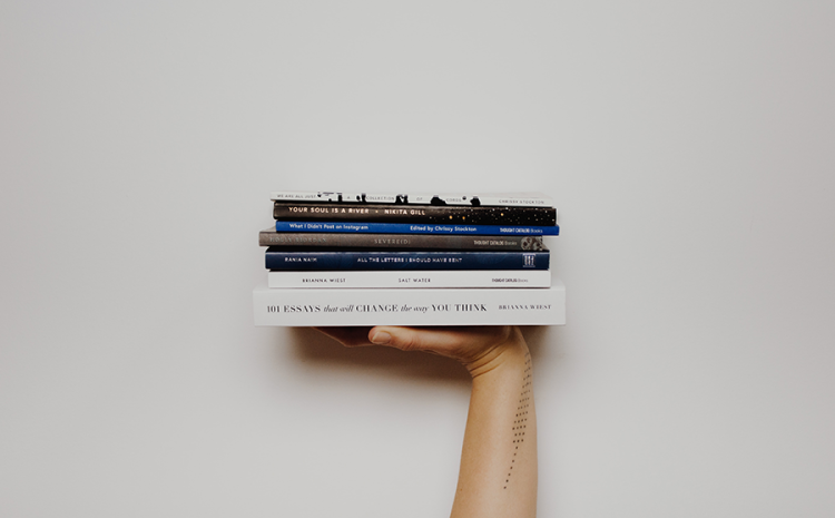 Person holding up a stack of various books